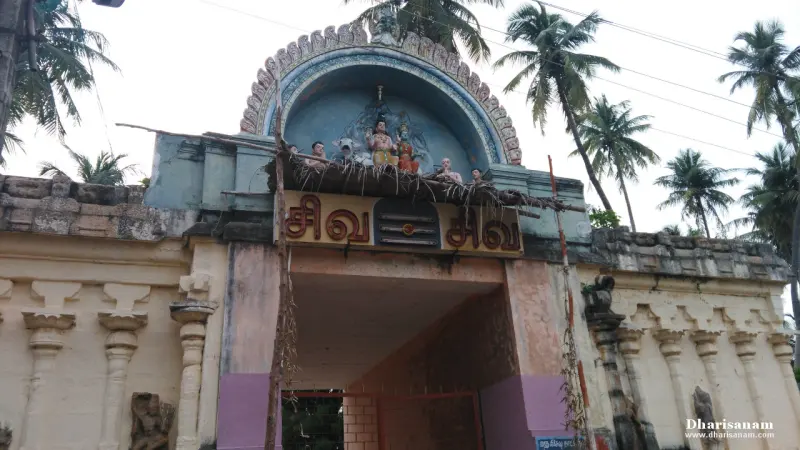 An entrance gateway under an arch with coloured figures of Shiva and Parvathy, a name board and palm trees