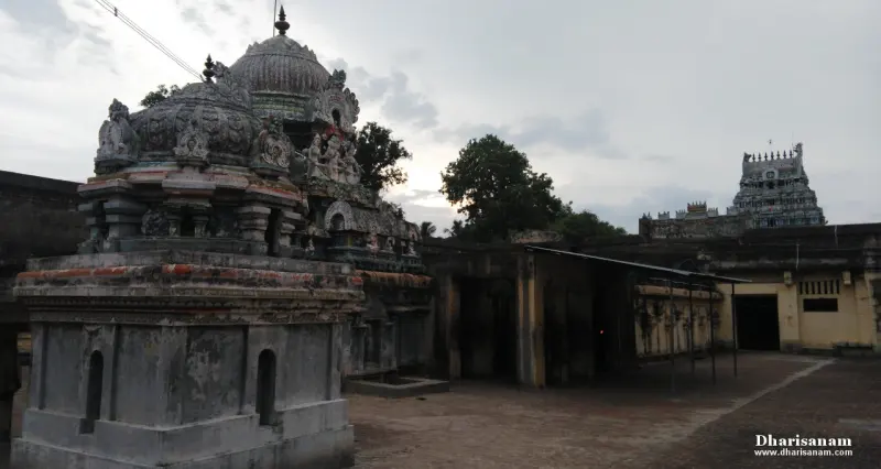 A weathered stone shrine tower with carved figures in a courtyard, and a tall painted tower in the distance.