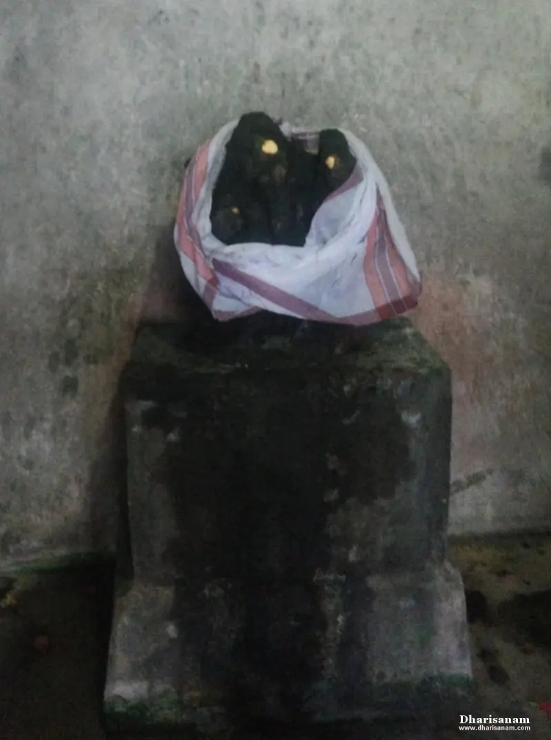 Dark stone figures with yellow marks, wrapped in a white cloth, rest on a stone pedestal.