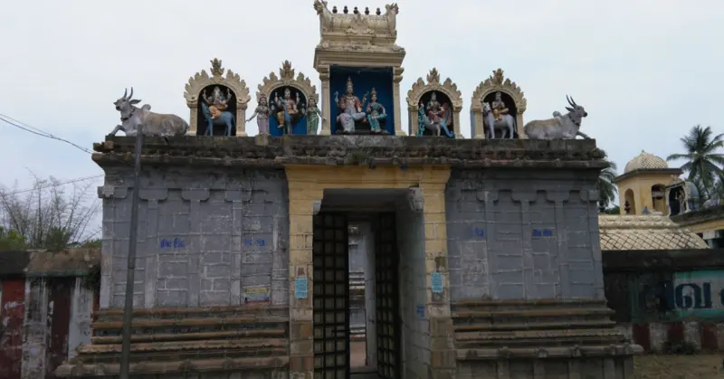 A grey stone gateway with a dark doorway, painted figures in arched niches and two bull statues on its roof.