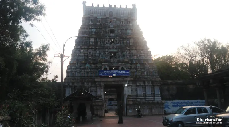 A tower with a blue name board over the gateway, with a street lamp and a parked car in front.