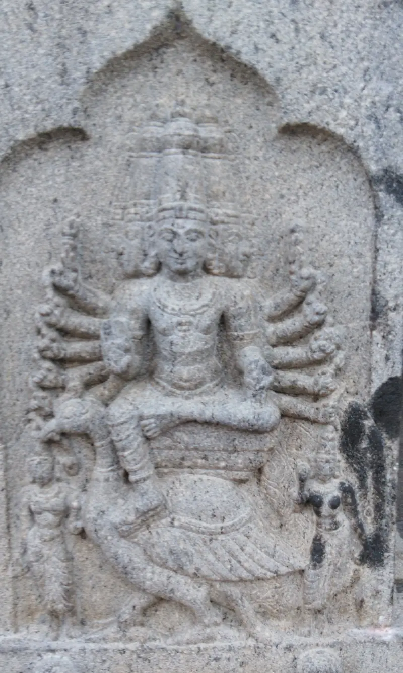 Stone relief of a crowned figure with many arms seated on a peacock