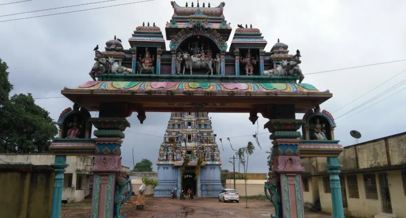 A painted entrance arch with sculpted figures on top; a tower stands behind it and a car is parked below.