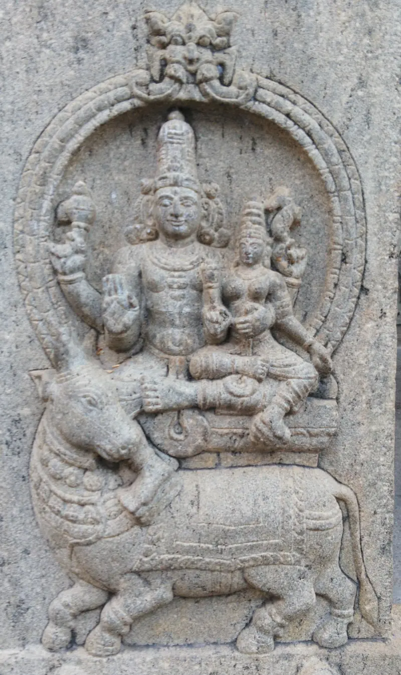 Stone relief of a seated couple with a bull below, inside a carved arch