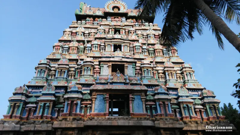A tall tiered gopuram in blue, green and red colours rising against a clear sky, with a palm frond at right