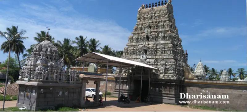 Carved stone tower beside a smaller tower, with palm trees and a shaded walkway below