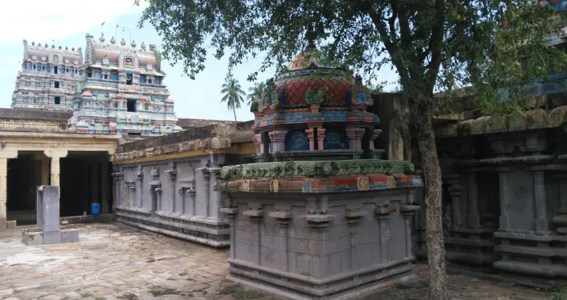 A domed shrine in a stone courtyard, the tall gopuram rising behind it