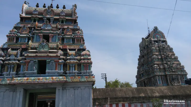 A colourful tower at left and an older carved stone tower at right, under a blue sky