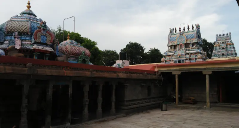 Stone courtyard with two domed shrine roofs on the left and painted towers beyond a pillared corridor